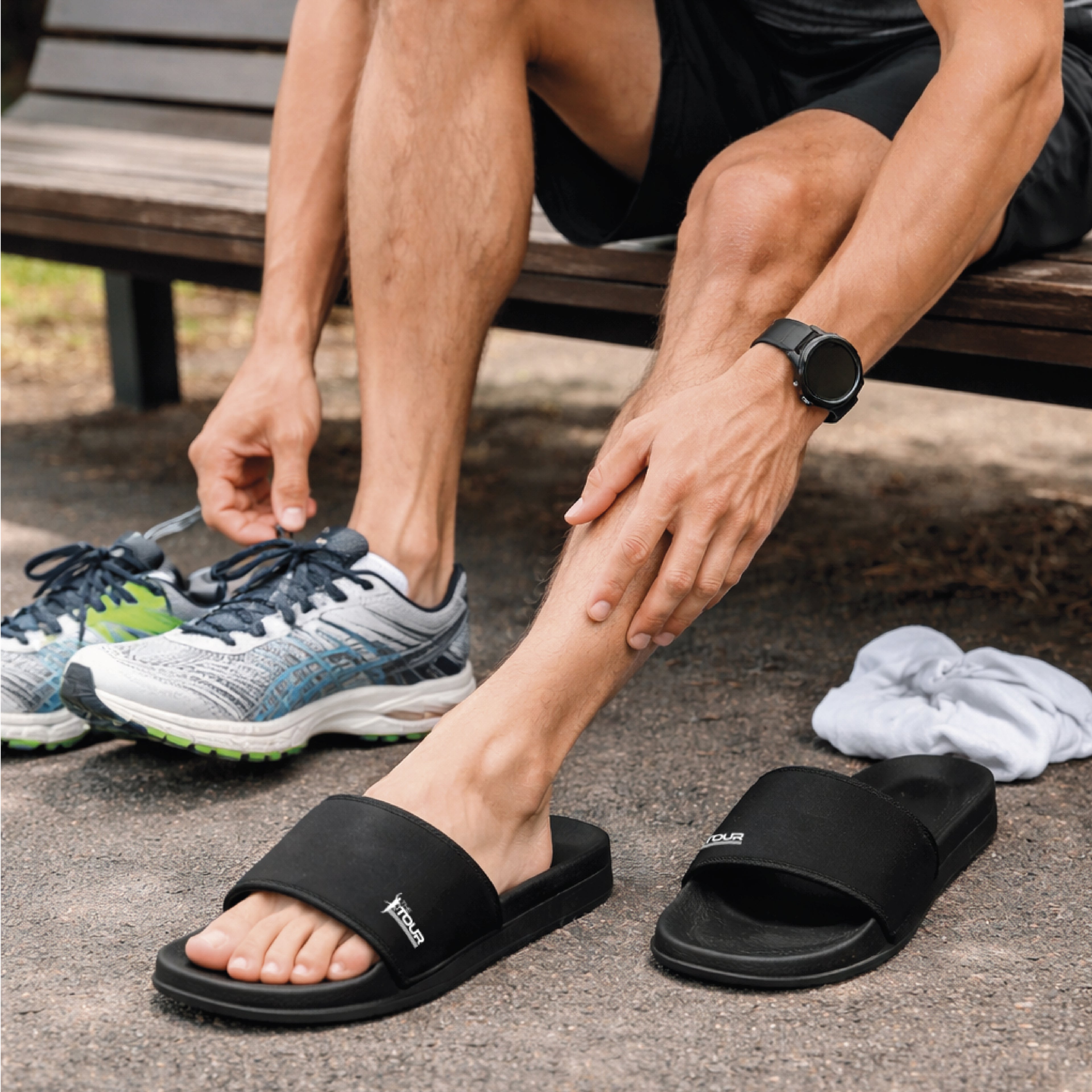 Person wearing black slides and switching to running shoes outdoors.